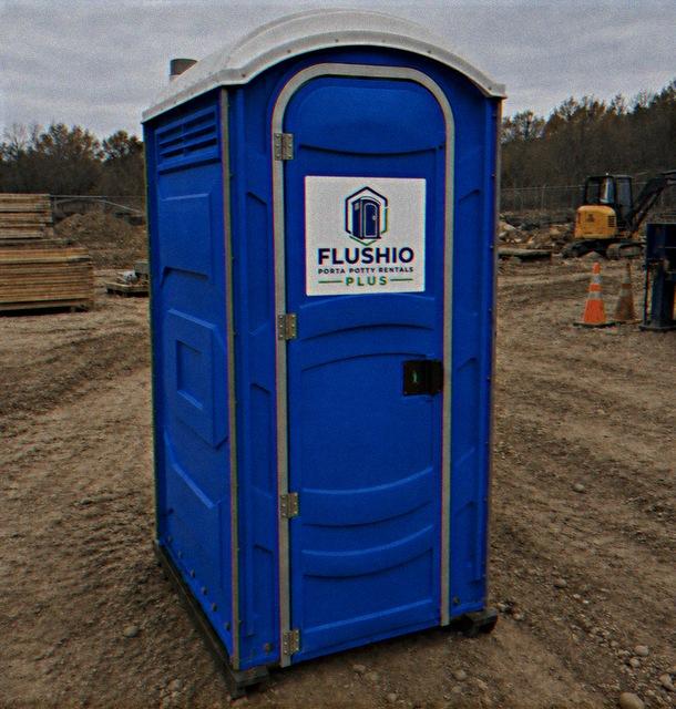 Portable toilet rental unit anchored on a construction site with lumber and machinery behind it