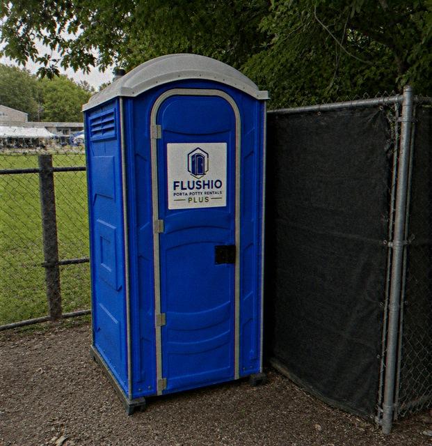 Portable toilet rental unit set along a fence line at an outdoor event